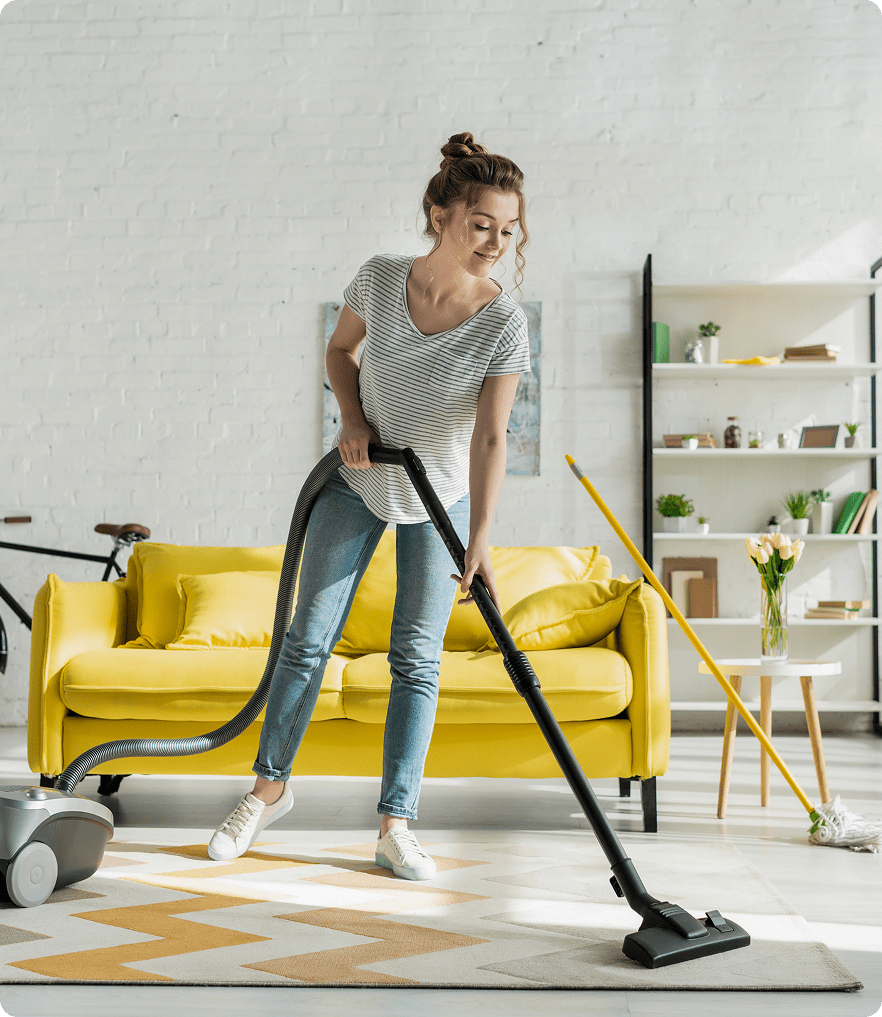 GettyImages-1455182972 (1) Woman vacuuming living room with yellow sofa.
