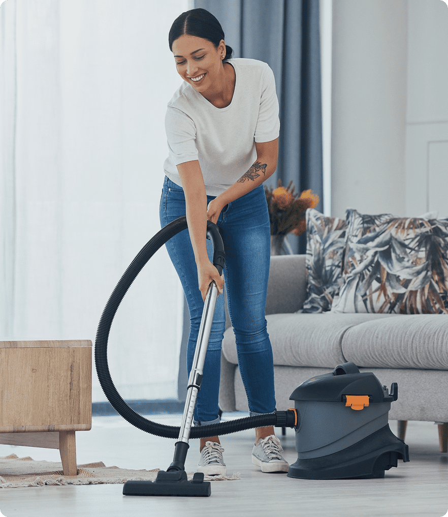 GettyImages-1455182972 Woman vacuuming living room floor, smiling.